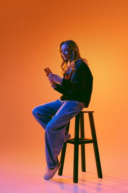 Profesyonel bir kadın stüdyodaki taburede otururken akıllı telefonu iş iletişimi için kullanıyor. İş mesajlarını kontrol etme, müşteri sohbetlerini yönetme ve günlük mobil görevleri yerine getirme kavramı.