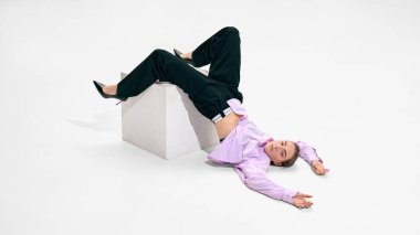 Lavanta gömlekli, beyaz küplü ve stüdyo arka planında siyah pantolonlu bir kadın yerde uzanıyor. Yaratıcı moda görünüm kitabı, cesur stil açıları ve mevsimsel giyim sunumu kavramı.