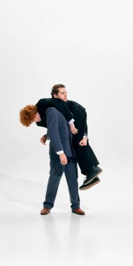 Stüdyoda iş arkadaşını sırtında taşıyan bir iş adamı. Beyaz arka planda koyu takım elbiseler giyiyor. Kurumsal baskı kavramı, takım sorumluluğu ve modern işyerindeki liderlik yükü.