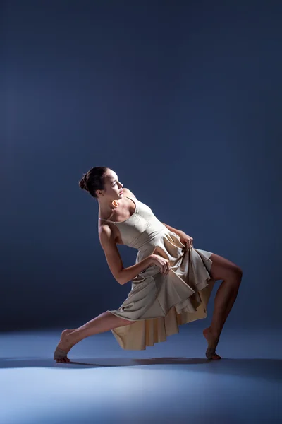 Jonge mooie danseres in beige jurk dansen op grijze achtergrond — Stockfoto