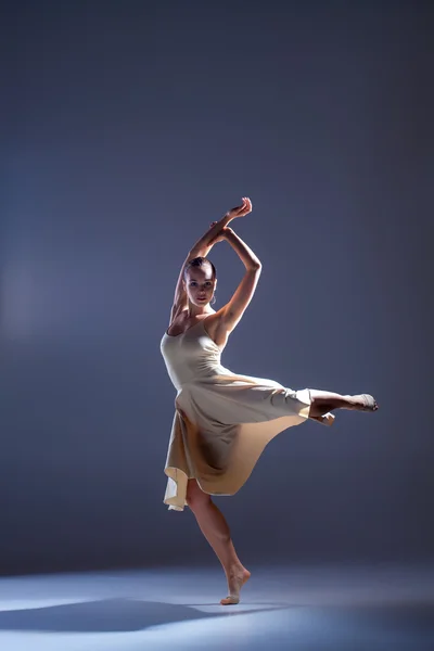 Jonge mooie danseres in beige jurk dansen op grijze achtergrond — Stockfoto