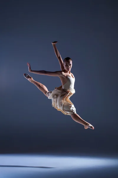 Молодая красивая танцовщица в бежевом платье прыгает на сером фоне — стоковое фото