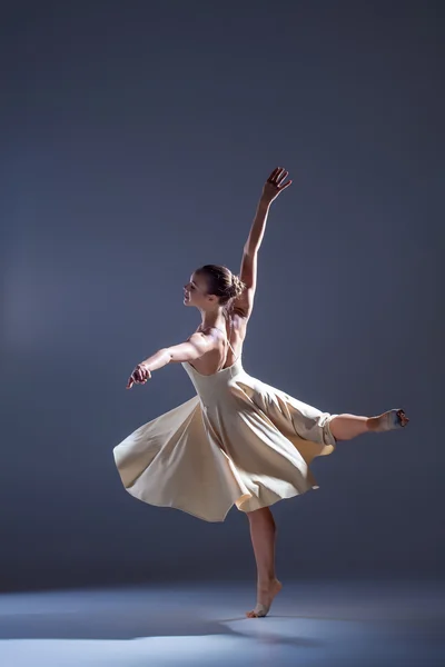 Jonge mooie danseres in beige jurk dansen op grijze achtergrond — Stockfoto