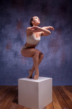 Young beautiful dancer in beige swimwear posing on white cube