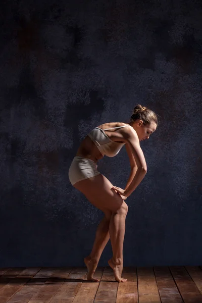 Молодая красивая танцовщица в бежевых купальниках танцует на сиреневом фоне — стоковое фото