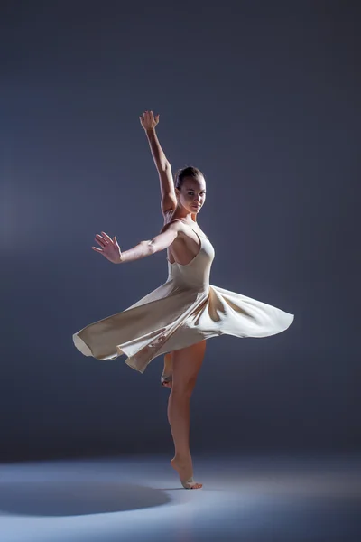 Jeune belle danseuse en robe beige dansant sur fond gris — Photo