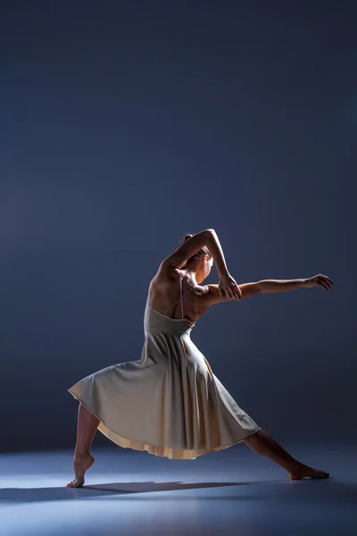 Jonge mooie danseres in beige jurk dansen op grijze achtergrond — Stockfoto