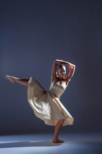 Junge schöne Tänzerin in beigem Kleid tanzt auf grauem Hintergrund — Stockfoto