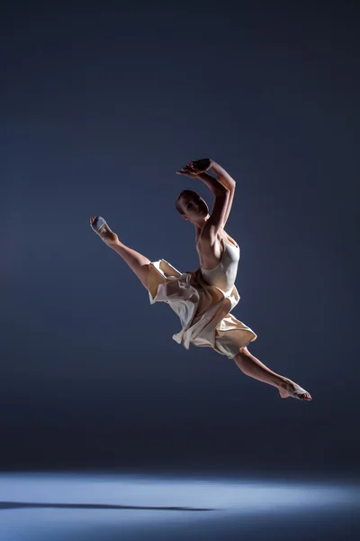 Jonge mooie danseres in beige jurk springen op grijze achtergrond — Stockfoto