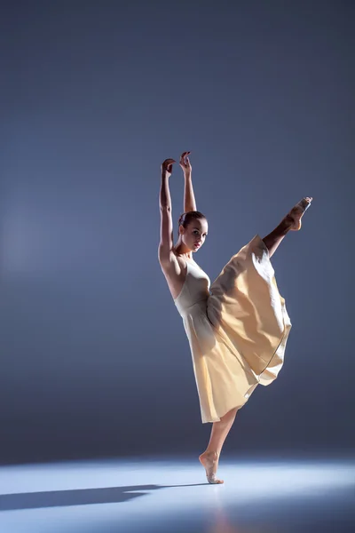 Молодая красивая танцовщица в бежевом платье танцует на сером фоне — стоковое фото