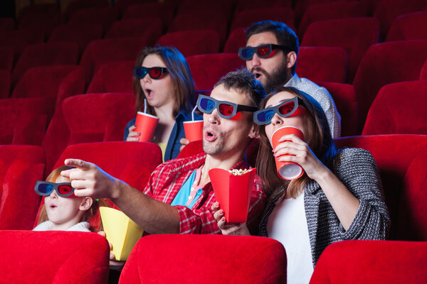 The spectators sitting in the cinema and watching movie  with cups of cola and popcorn. Concept of a variety of human emotions