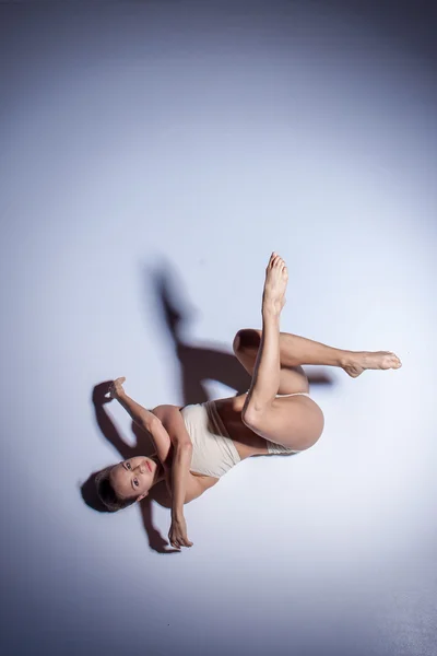 Молодая красивая танцовщица в бежевых купальниках танцует на сиреневом фоне — стоковое фото