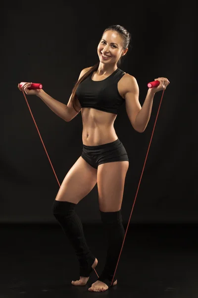 Мускулистая молодая спортсменка с скакалкой на черном — стоковое фото