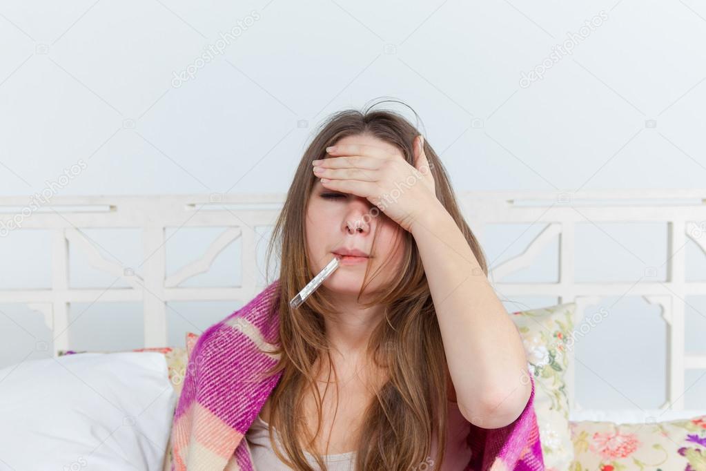 Young sick woman in blanket with thermometer