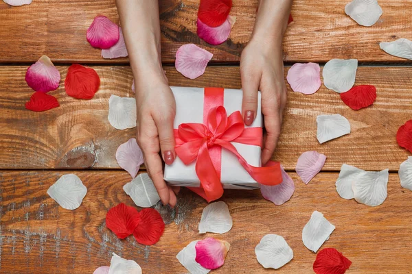 Regalo de San Valentín y manos femeninas sobre fondo de madera con pétalos — Foto de Stock