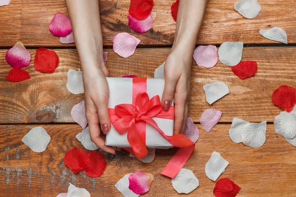 Regalo de San Valentín y manos femeninas sobre fondo de madera con pétalos — Foto de Stock