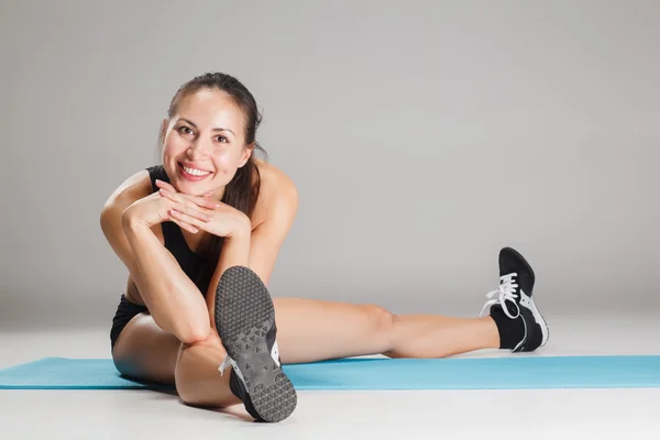 Musculosa joven atleta estirándose sobre gris —  Fotos de Stock