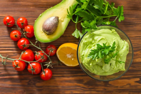 Guacamole on wooden table surrounded by its ingridients — Stock Photo, Image
