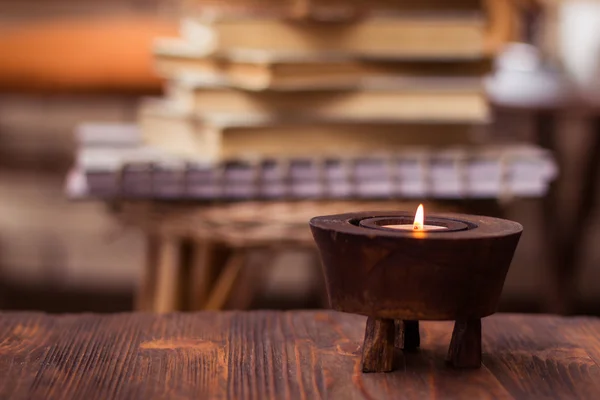 Candle on wooden table with books in background — Stock Photo, Image