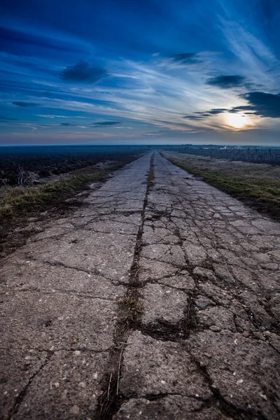 Поврежденная дорога в сельской местности с прекрасным закатом — стоковое фото