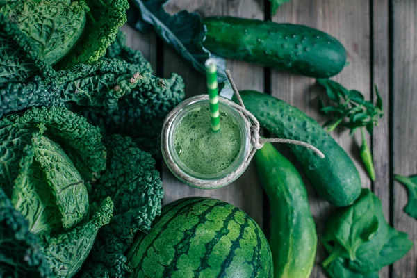 Ahşap masadaki malzemelerle harmanlanmış yeşil smoothie.