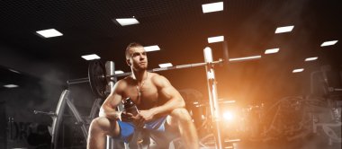 Young muscular man sitting with a bottle of water in the gym