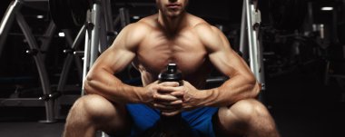 Young muscular man sitting with a bottle of water in the gym