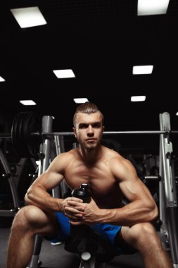 Young muscular man sitting with a bottle of water in the gym