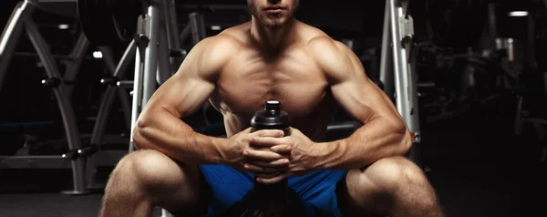 Young muscular man sitting with a bottle of water in the gym — Stock Photo, Image