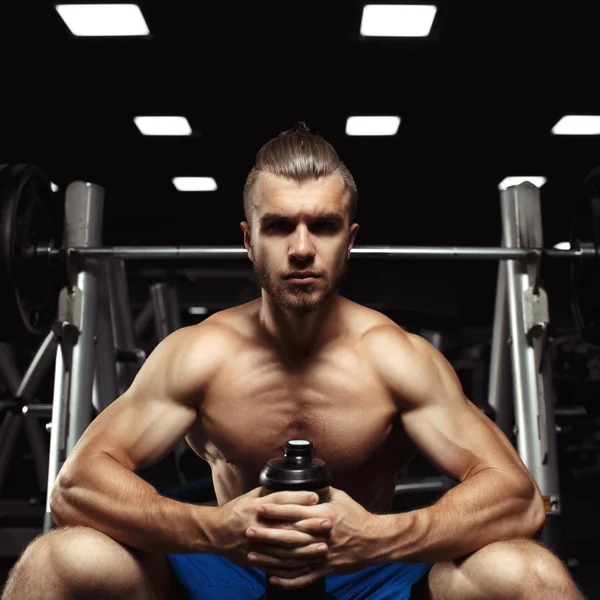 Junger muskulöser Mann sitzt mit einer Flasche Wasser in der Turnhalle — Stockfoto