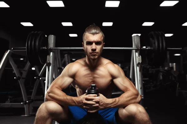 Junger muskulöser Mann sitzt mit einer Flasche Wasser in der Turnhalle — Stockfoto