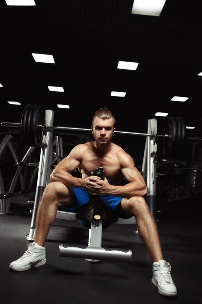 Giovane uomo muscoloso seduto con una bottiglia d'acqua in palestra — Foto Stock