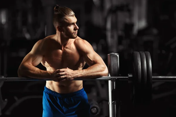 Attractive muscular bodybuilder guy prepare to do exercises with barbell in a gym — Stock Photo, Image