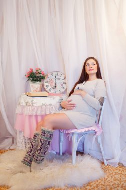 Güzel bir hamile kadın bir sandalyede oturuyor ve beline sarılarak