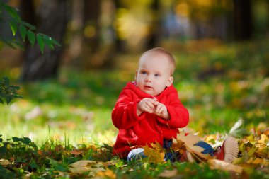 Kırmızı elbiseli sarı yaprakları ile oynayan neşeli bebek