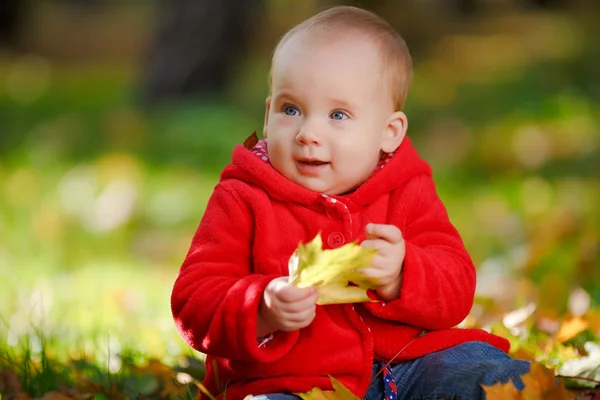 Веселый младенец в красном платье играет с желтыми листьями — стоковое фото