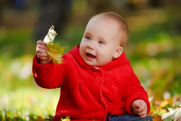 Cheerful baby in a red dress playing with yellow leaves — Stock Photo, Image