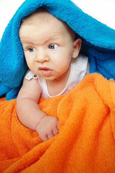 Bébé adorable de deux mois et demi, regardant sous une couverture ou une serviette bleue et orange — Photo