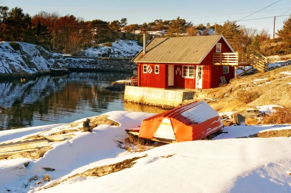 Rode rorbu op rotsachtige kust, rond rotsen bedekt met sneeuw — Stockfoto