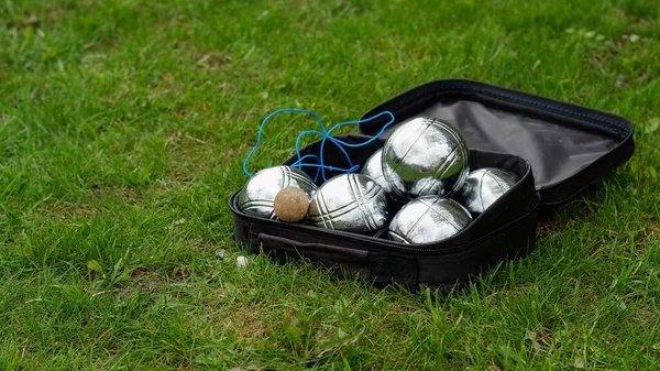 Petanque set with six metal balls and a measuring rope in a black case on green grass. Play in your own garden during quarantine.
