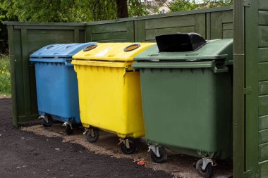 Çitin yanında çöp dolu üç plastik renkli konteynır. Atık ayıklama ve ev atıklarının toplanması. Çevreye karşı sorumlu tutum. Sıfır atık.