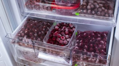 The frozen cherries in the freezer are packed in plastic boxes and plastic bags. Open freezer with frozen red cherries. Food storage. Frozen food. Stocks of products for the quarantine period.