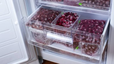 The frozen cherries in the freezer are packed in plastic boxes and plastic bags. Open freezer with frozen red cherries. Food storage. Frozen food. Stocks of products for the quarantine period.