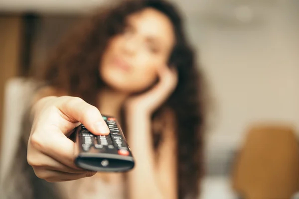 Chica sosteniendo un control remoto de TV, cambiando el canal . Imagen de archivo