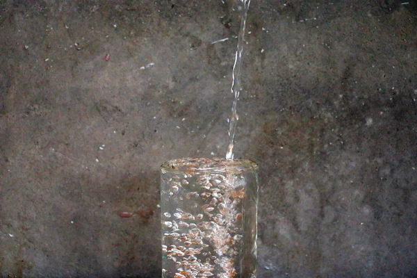 Effet de la goutte d'eau et du verre d'eau sur la table en bois devant le fond du mur de ciment — Photo