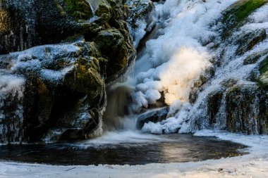 Kışın çok güzel donmuş bir şelale. Donmuş su ve her yer buz. İnanılmaz buz oluşumları. Ormanda parlayan ışık huzmeleri