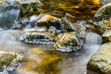Kışın güzel bir şelale. Buzla kaplı kayalar, suyun etrafını sarar.   