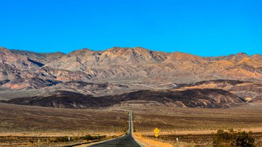 Death Valley Ulusal Parkı 'nın güzel manzarası. Yol görünüyor. Turuncu tepeler ve mor tonlu dağlar