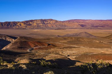 Death Valley Ulusal Parkı 'nın güzel manzarası. Yol görünüyor. Turuncu tepeler ve mor tonlu dağlar