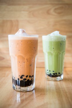 Aisian tarzı yeşil ve turuncu köpüklü çay, üstünde süt köpüğü olan ahşap bir arka plan.